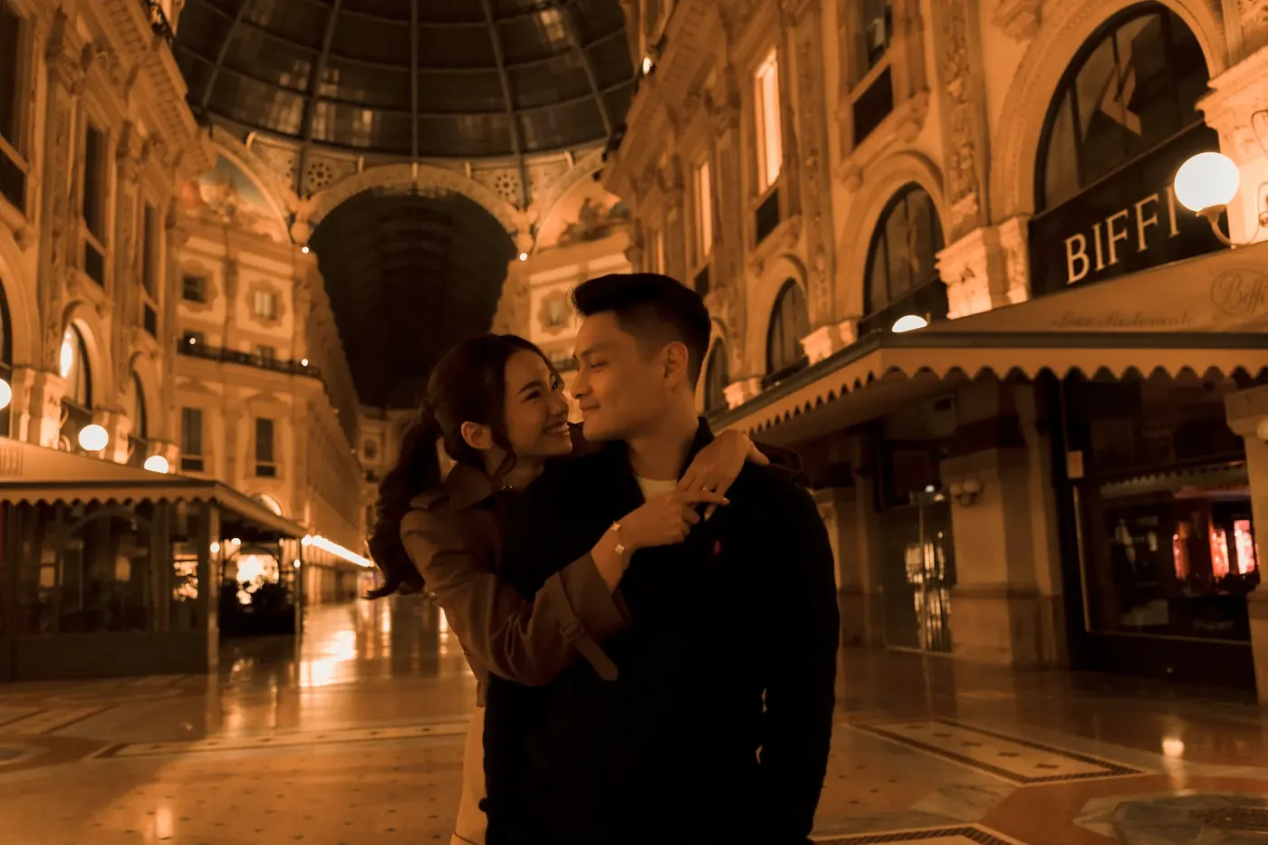 Matthew and Karin embracing in a glowing, arcaded galleria at night