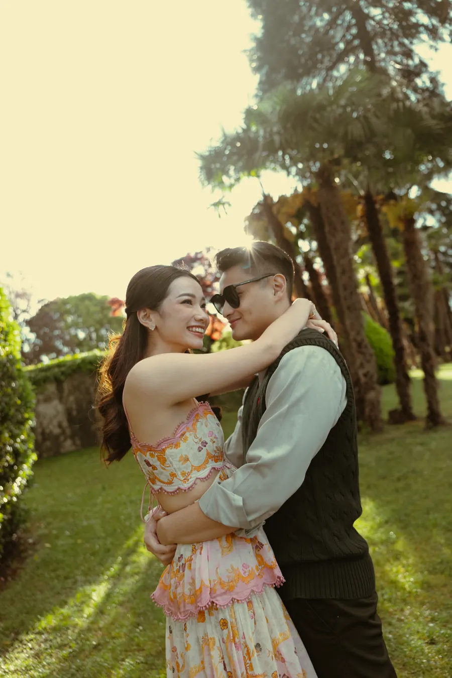 Karin in a floral dress embracing Matthew beneath tall trees